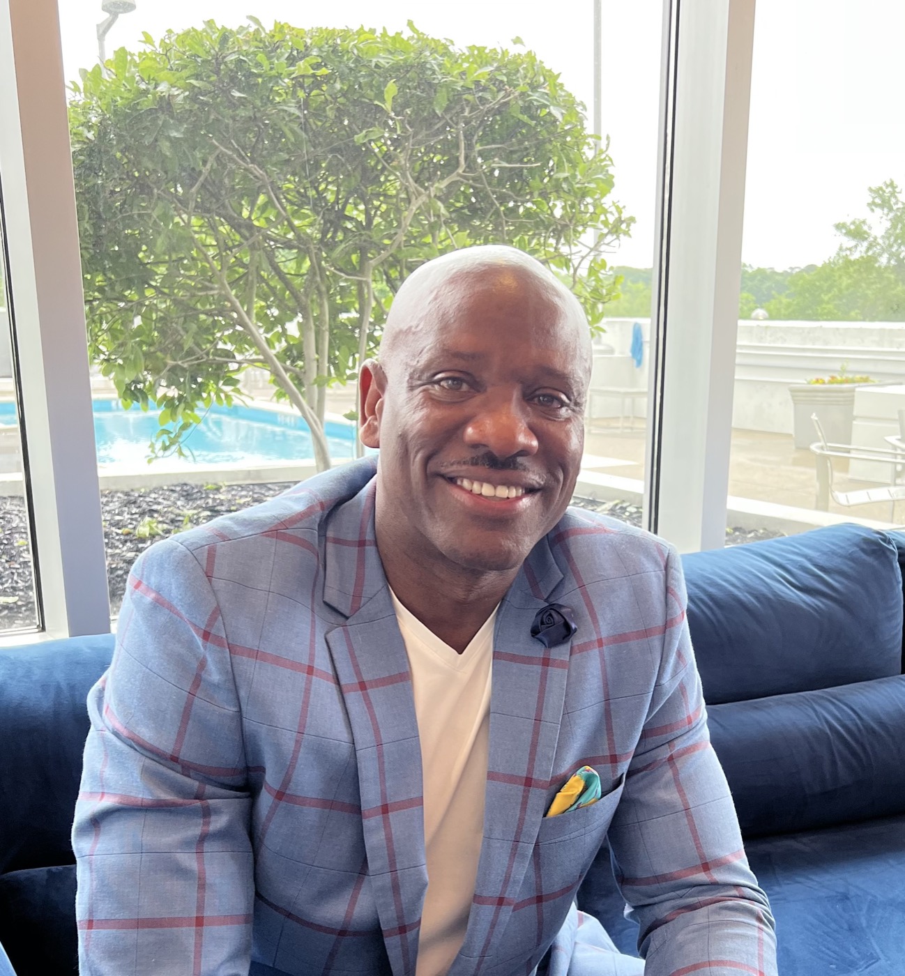 Mr. Tycoon, smiling, in a plaid blazer on a navy sofa